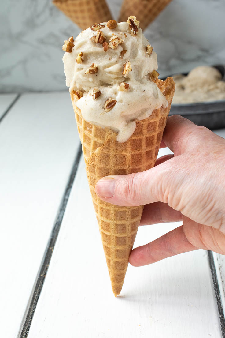 Holding a waffle cone with banana ice cream topped with chopped pecans