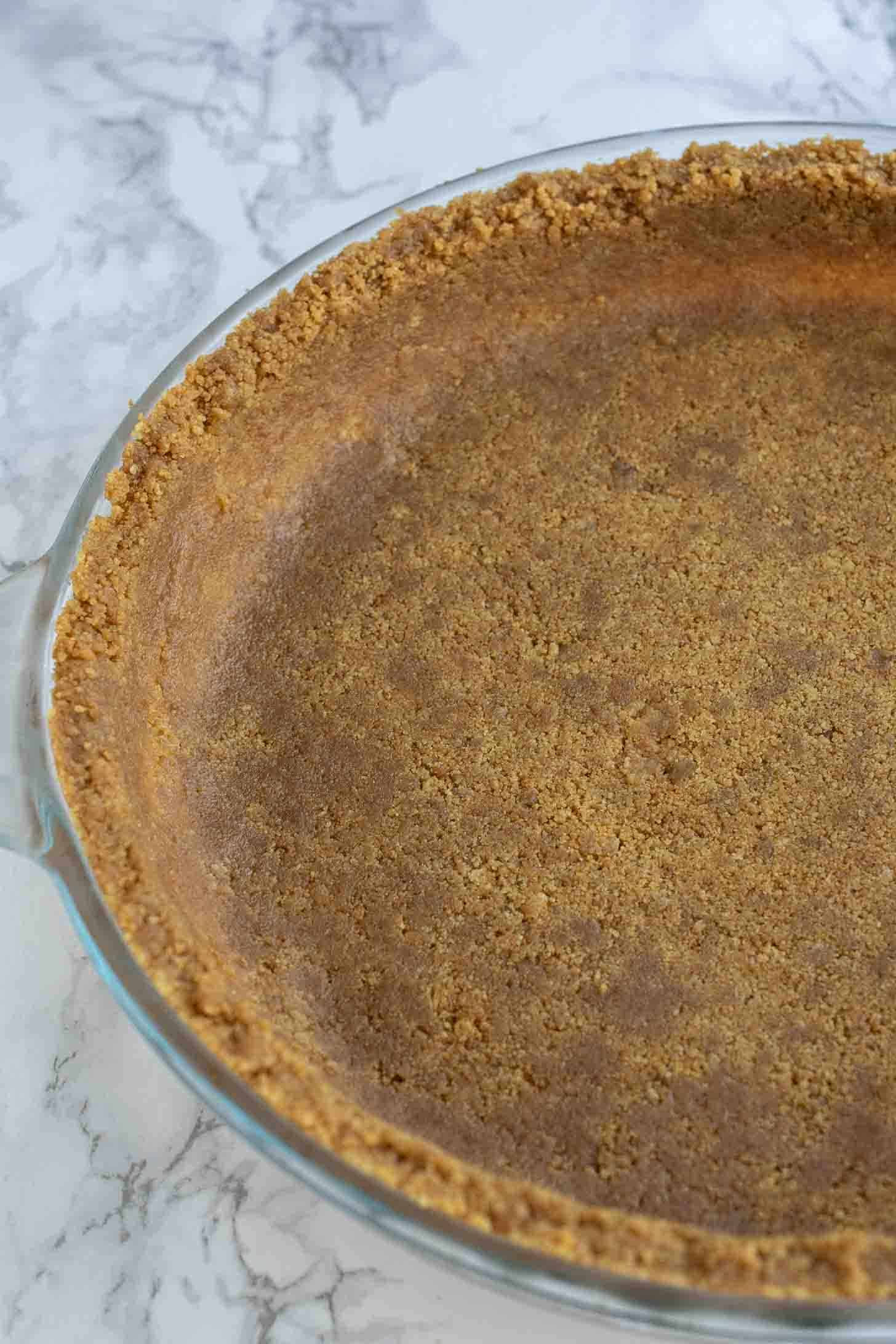A closeup of gingersnap cookie crumbs pressed into a pie pan to create a pie crust