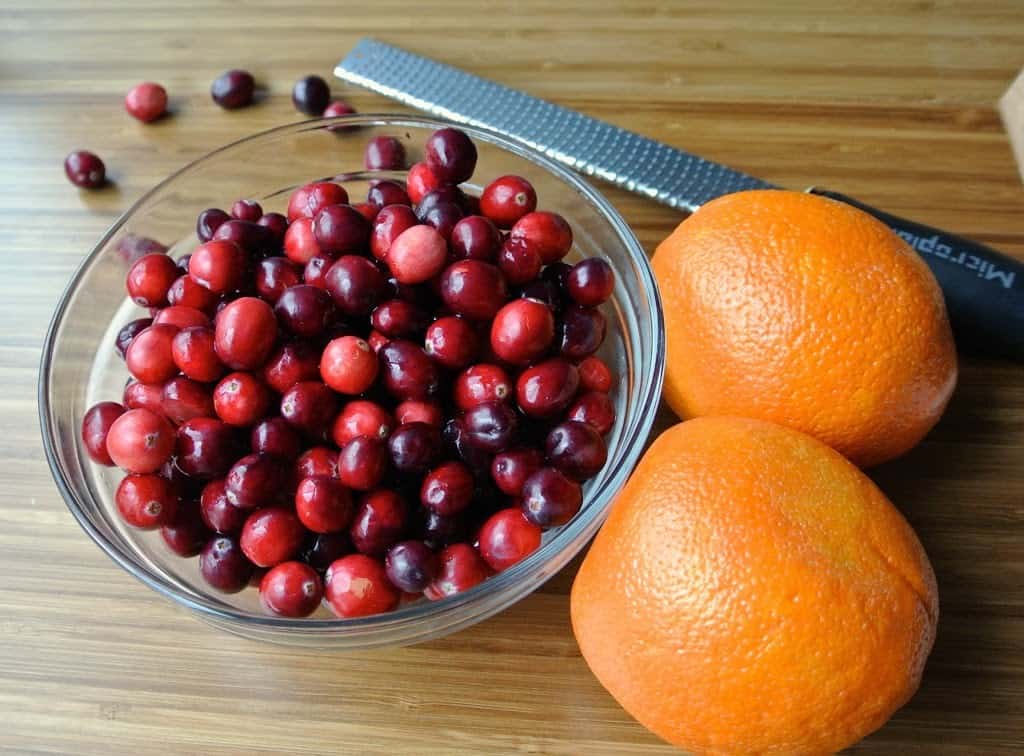 A bowl of fresh cranberries with 2 whole oranges and a zester