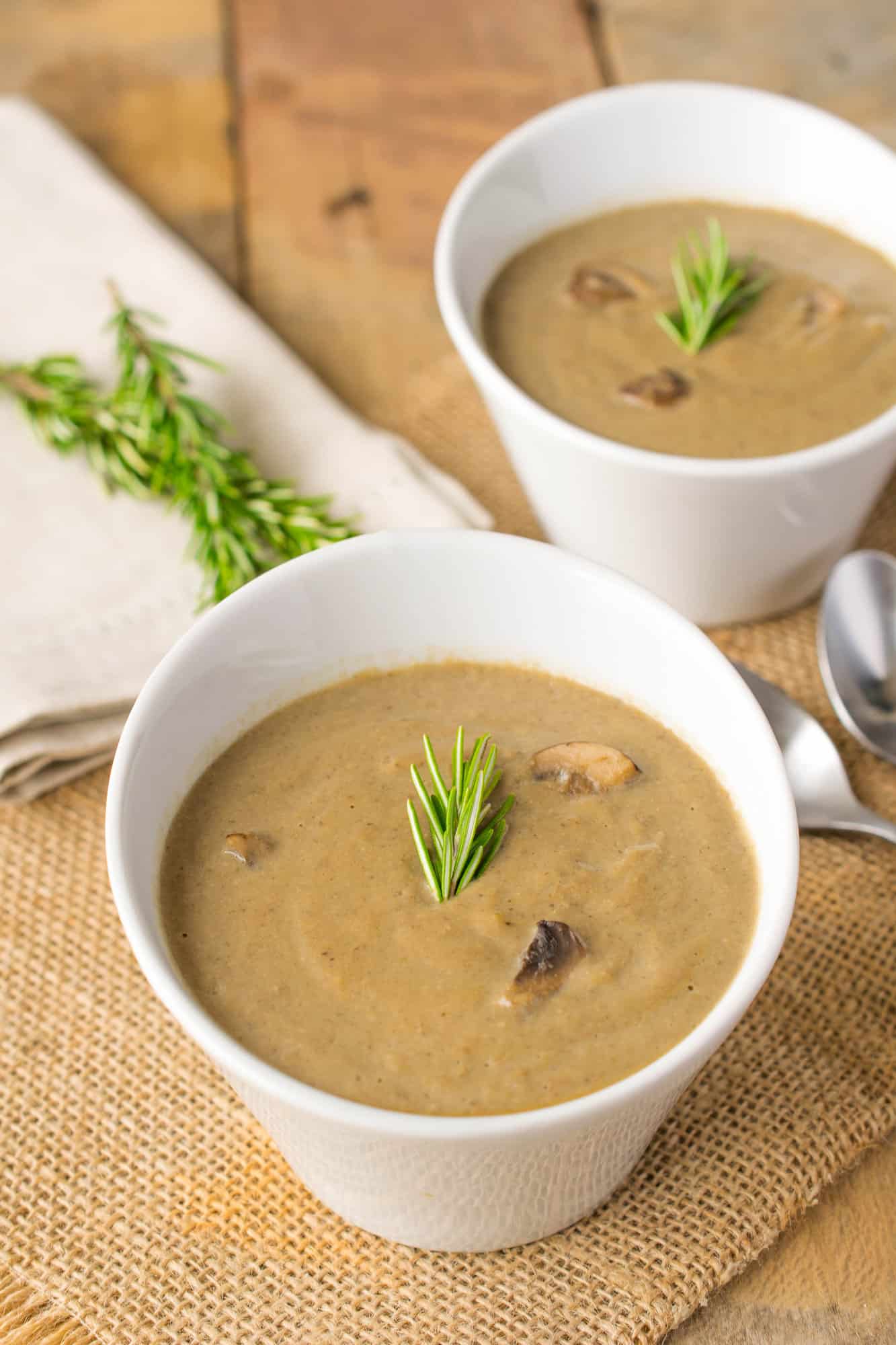 Vegan mushroom soup served in decorative white bowls garnished with fresh rosemary