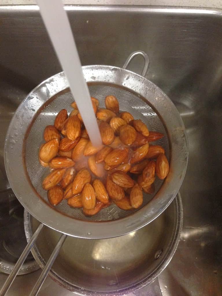 Boiled almonds being rinsed under water