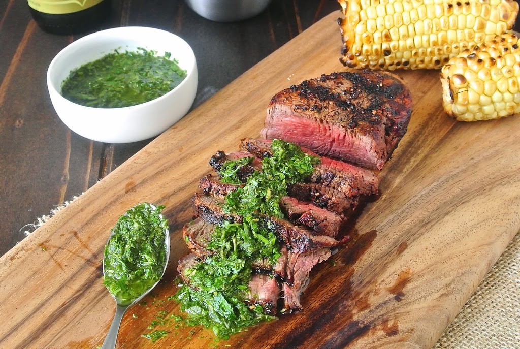 Grilled filet mignon with mint and parsley served on a cutting board with grilled corn on the cob