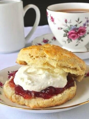 A flowered plate with a scone, jam and clotted cream and a cup of tea in the background