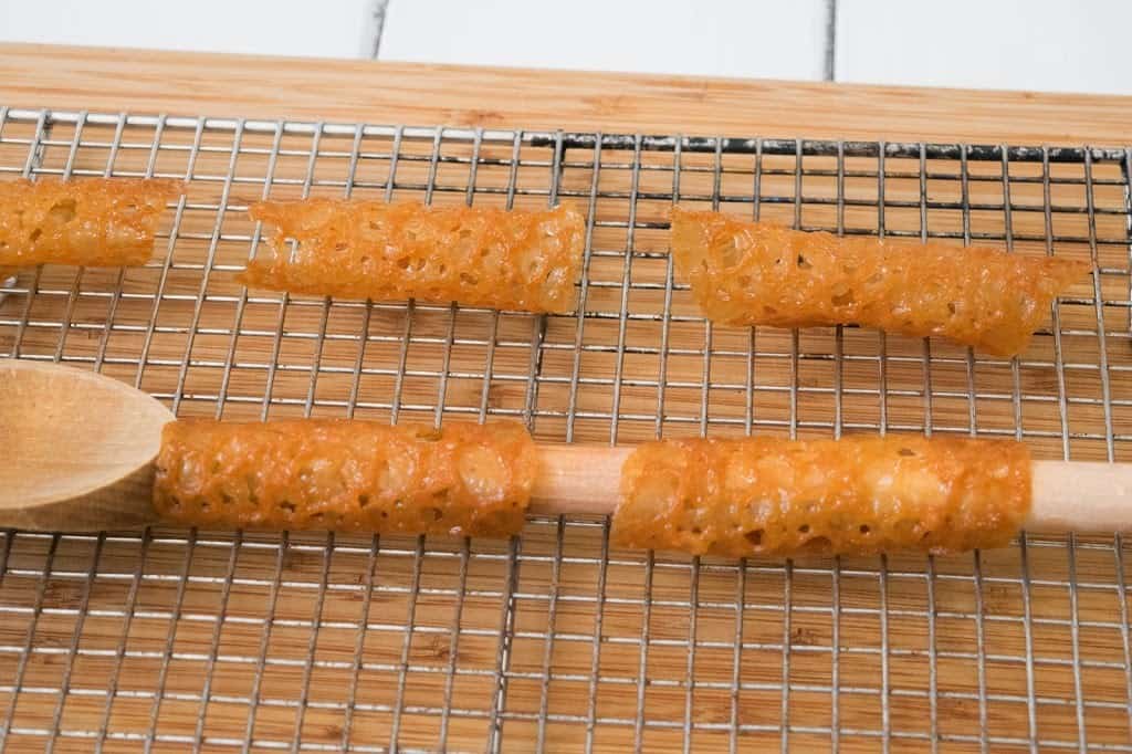 Lace cookies shaped into tubes around a wooden spoon