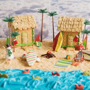 2 beach houses made out of graham crackers on a beach of graham cracker sand and blue frosting ocean