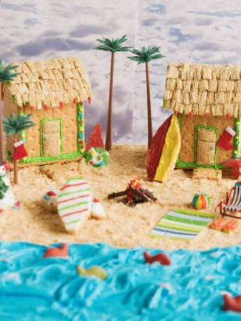 2 beach houses made out of graham crackers on a beach of graham cracker sand and blue frosting ocean
