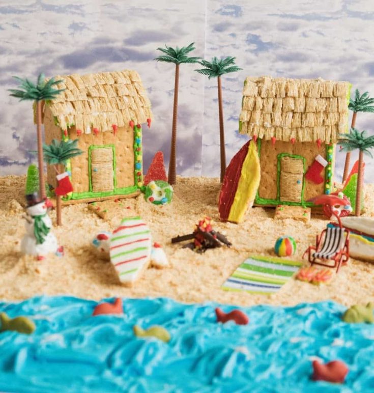 2 beach houses made out of graham crackers on a beach of graham cracker sand and blue frosting ocean