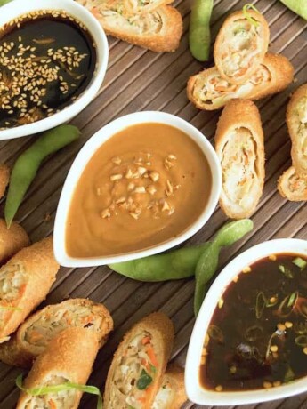 Asian sauces in white bowls in a diagonal line with egg rolls
