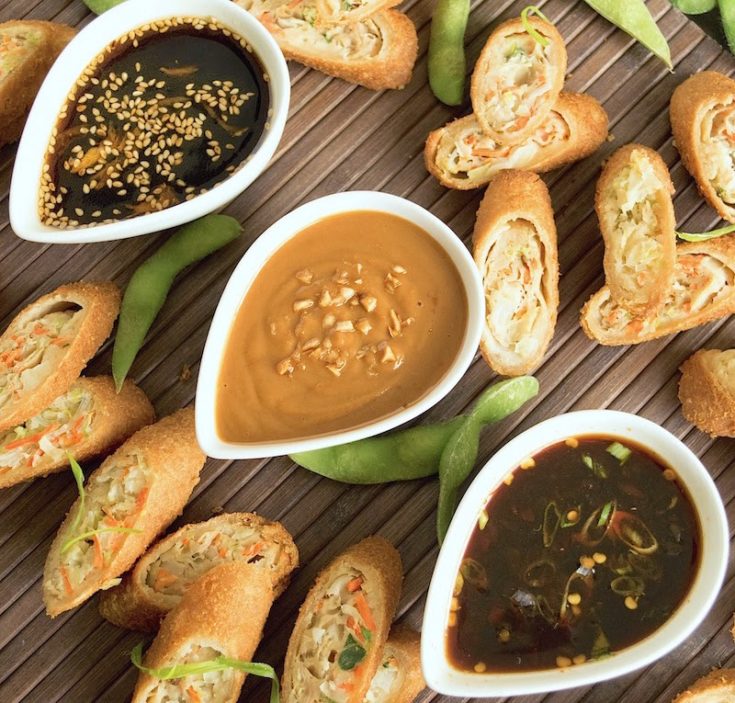 Asian sauces in white bowls in a diagonal line with egg rolls
