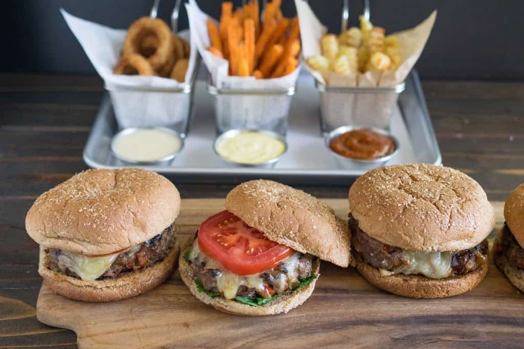3 burgers on a board with French fries and onion rings