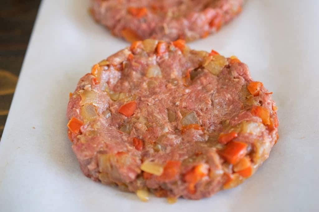 A closeup of a burger pattie showing the pepper and onion in the meat