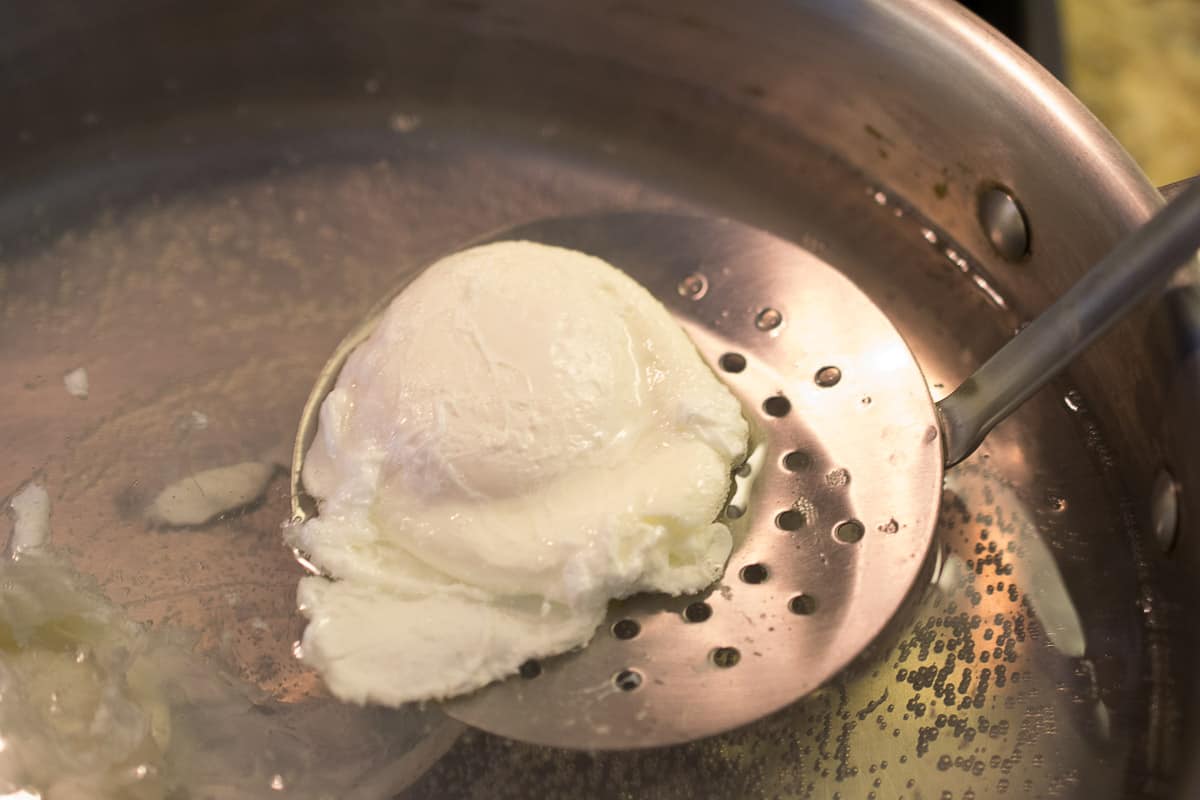 Removing a poached egg from a pan of water with a slotted spoon