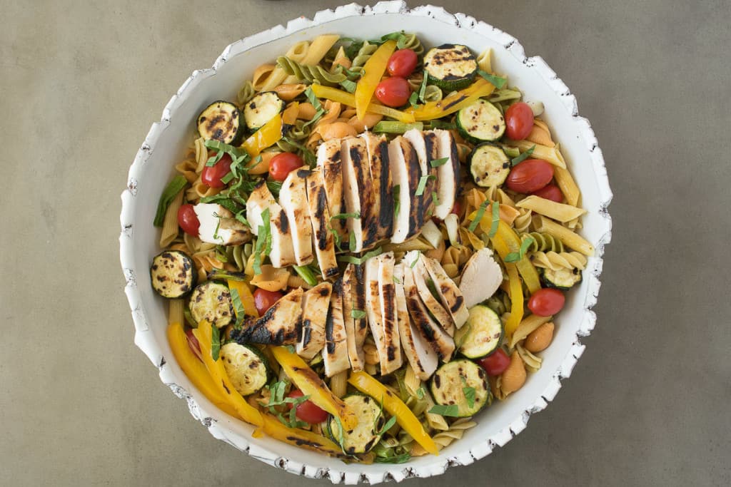 Pasta, grilled chicken and vegetables in a white bowl
