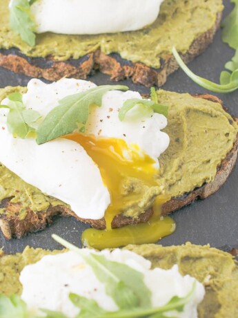 A poached egg on avocado artichoke toast cut open with yolk running out
