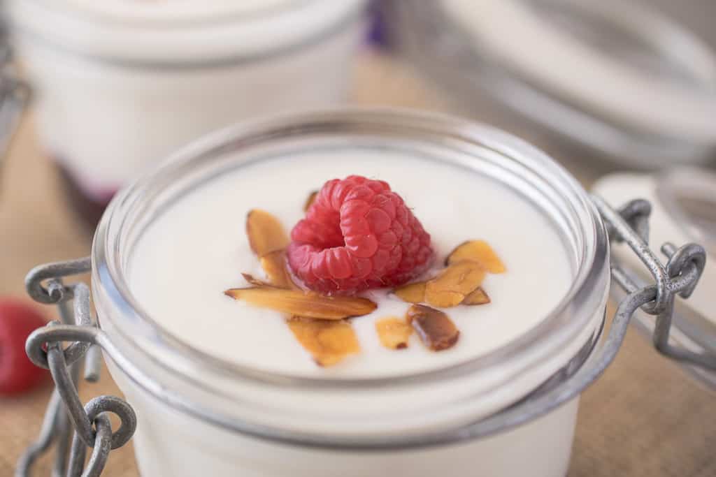 A closeup of a raspberry on top of the yogurt with toasted almonds