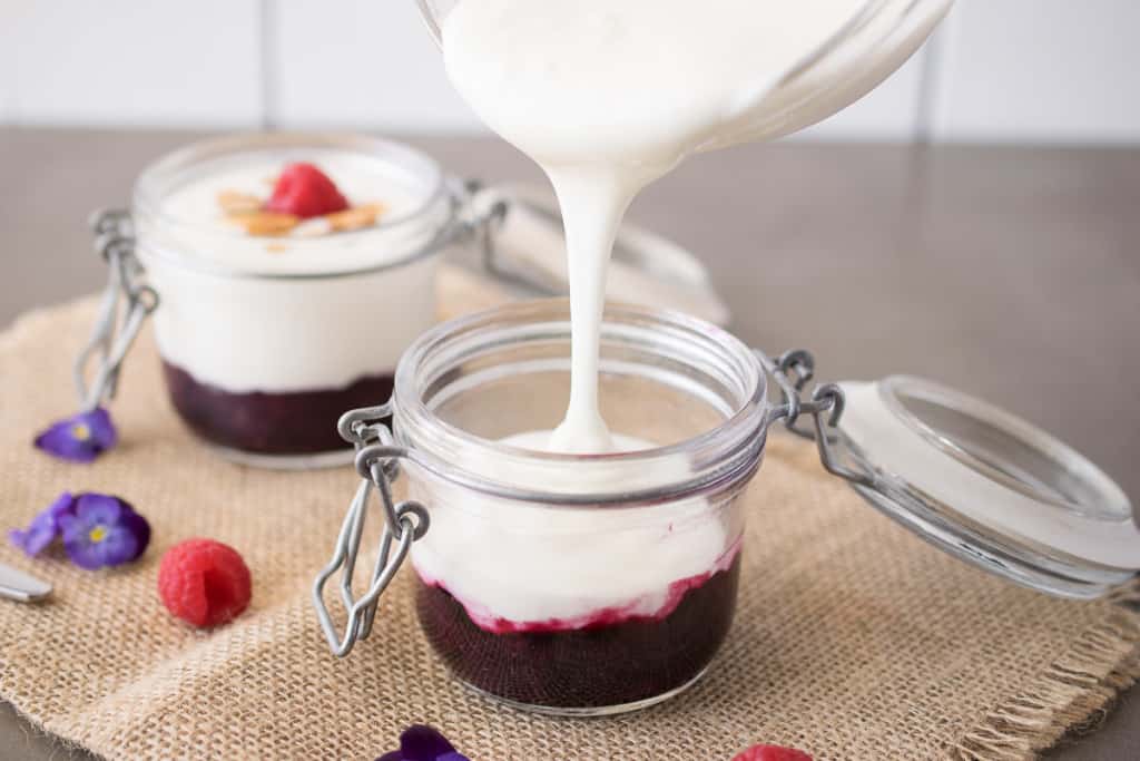 A jar with blueberry sauce with yogurt being pour in