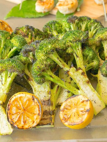 Grilled broccoli with lemon slices on a serving board
