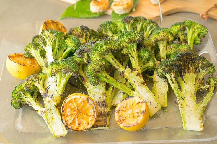 Grilled broccoli with lemon slices on a serving board