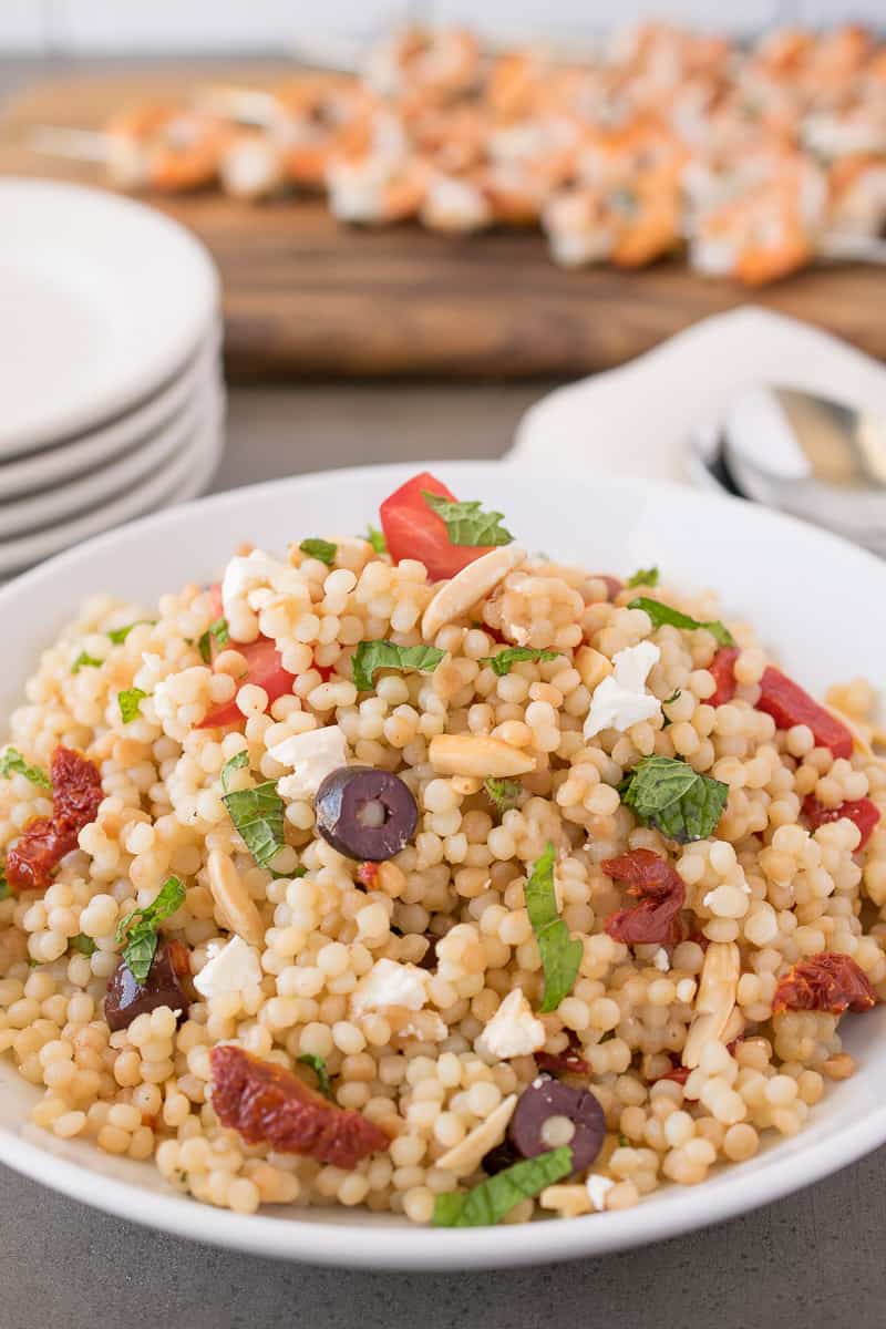 Mediterranean couscous salad served in a white bowl with olives, sun-dried tomatoes and basil