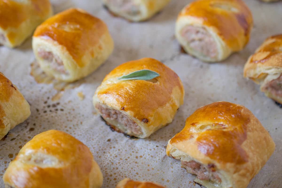 A closeup of mini sausage rolls on a baking sheet fresh out of the oven