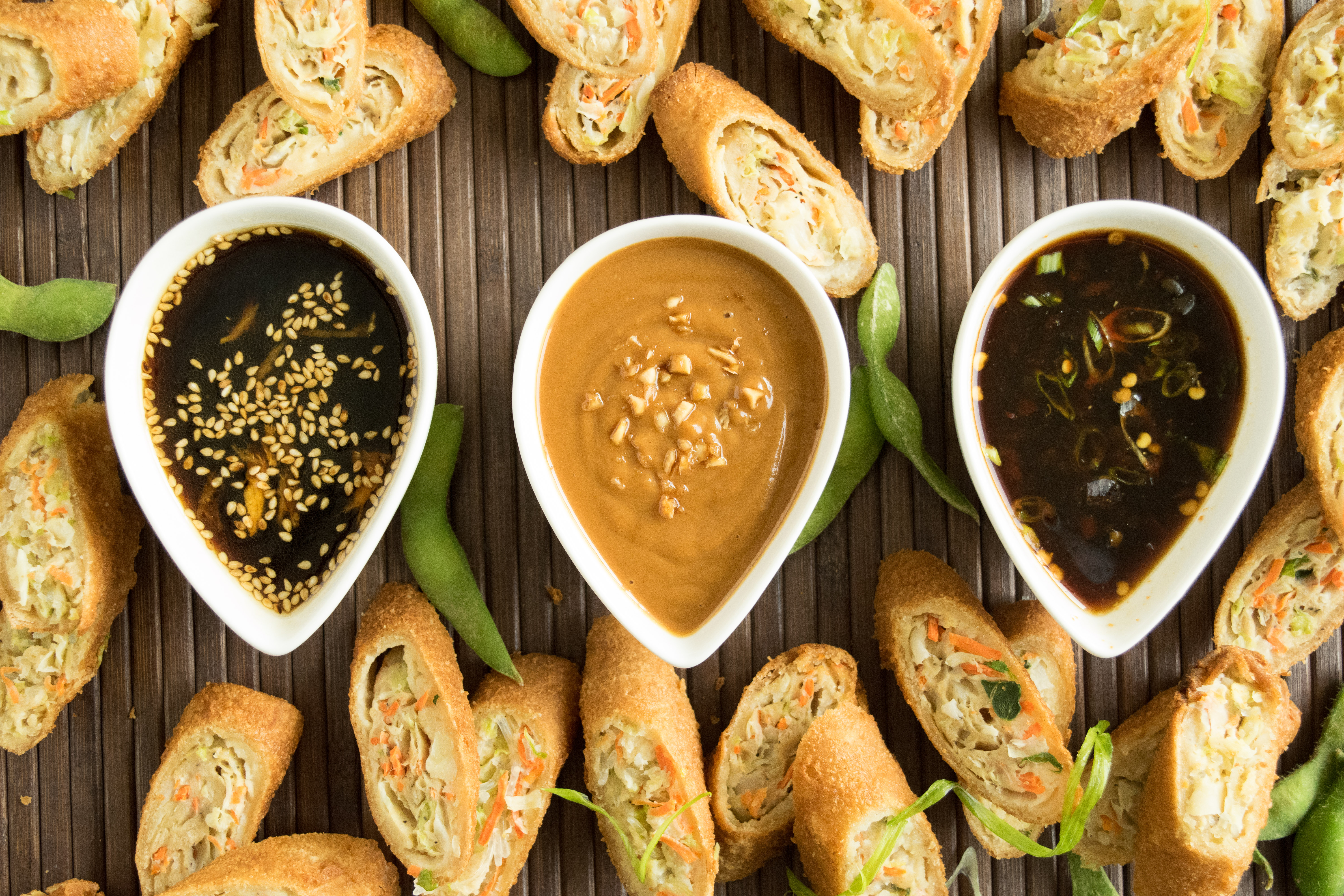 Asian sauces lined up in white bowls surrounded by egg rolls