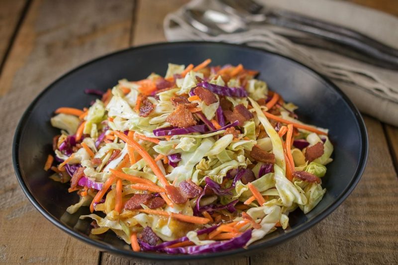 A closeup showing the red cabbage, green cabbage, orange carrot and crispy bacon