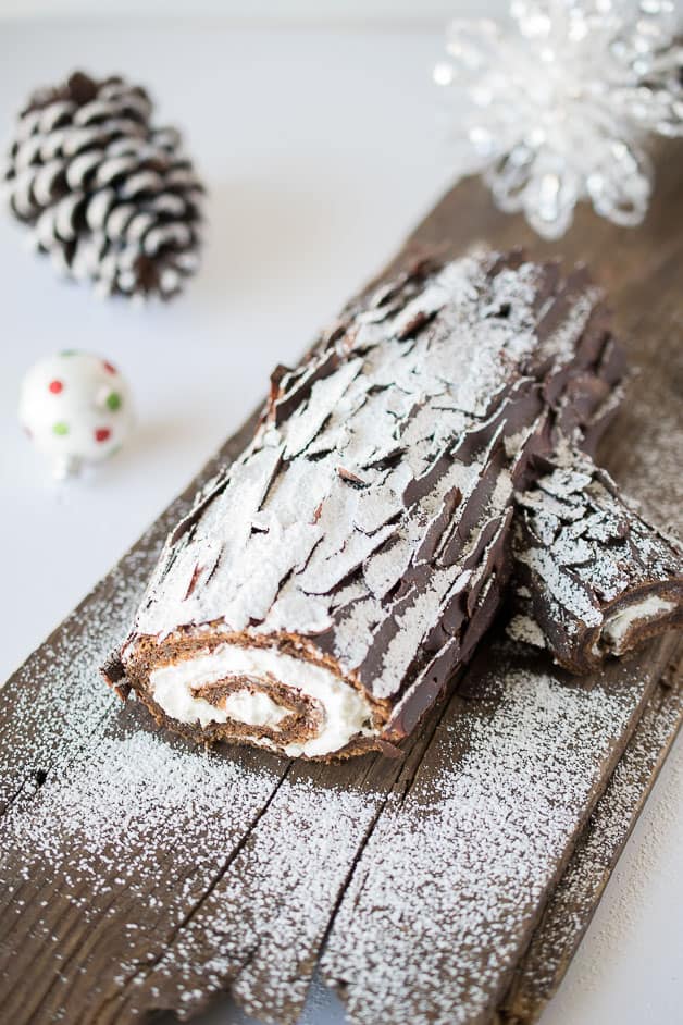 The Yule log on a wood plank dusted with powdered sugar to look like snow with a pine cone