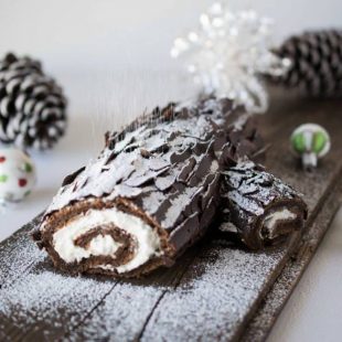A Yule log on a plank of wood being dusted with powdered to sugar