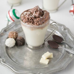 White hot chocolate with dark chocolate whipped cream on a pewter plate with chocolate dipped spoons and chocolate treats