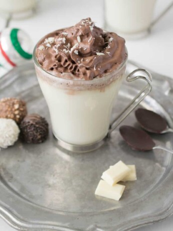 White hot chocolate with dark chocolate whipped cream on a pewter plate with chocolate dipped spoons and chocolate treats