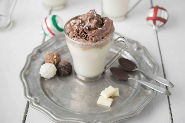 White hot chocolate with dark chocolate whipped cream on a pewter plate with chocolate dipped spoons and chocolate treats