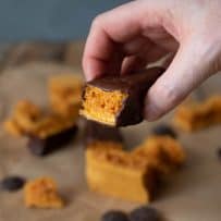 Holding a piece of 3 Ingredient Cinder Honeycomb Toffee coated in chocolate