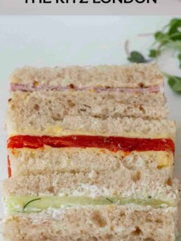 Small finger sandwiches without crusts with ham, smoked salmon and cucumber lined up on a plate