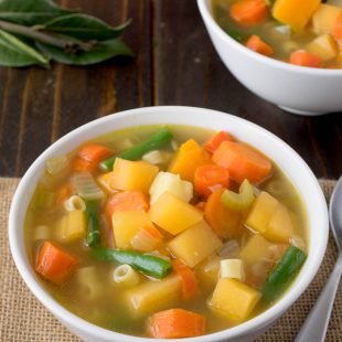 2 white bowls filled with vegetable soup with colors of yellow, orange and green