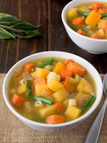 2 white bowls filled with vegetable soup with colors of yellow, orange and green