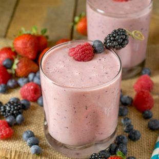 2 glasses of a berry healthy smoothie surrounded by berries