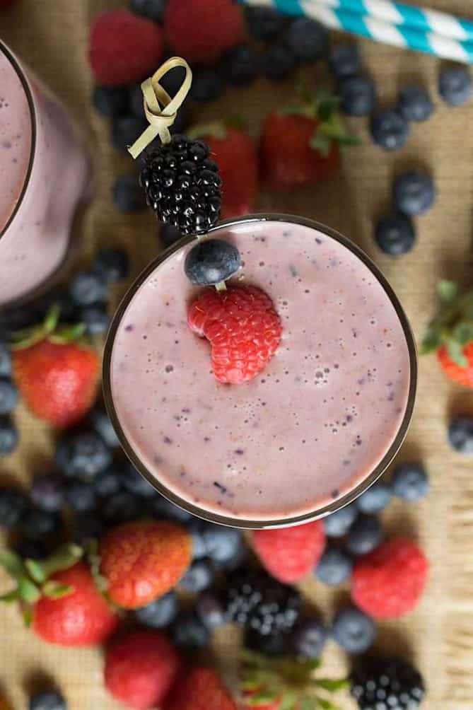 A berry healthy smoothie viewed from overhead surrounded by strawberries, blueberries and blackberries