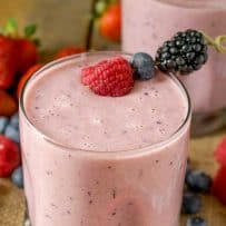 Flecks of colorful fruit can be seen in this pink smoothie in a glass garnished with skewered berries