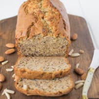 Banana bread sliced on a board with almonds and knife