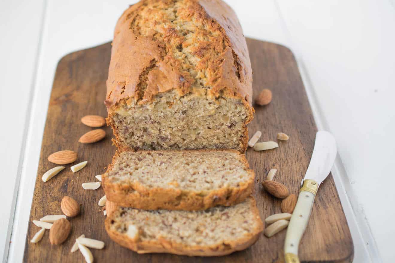 Banana bread sliced on a board with almonds and knife