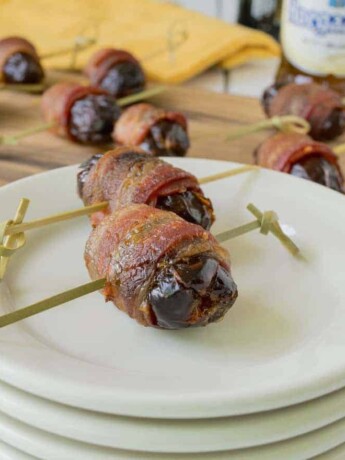 Apple stuffed bacon wrapped dates on white plates with more in background