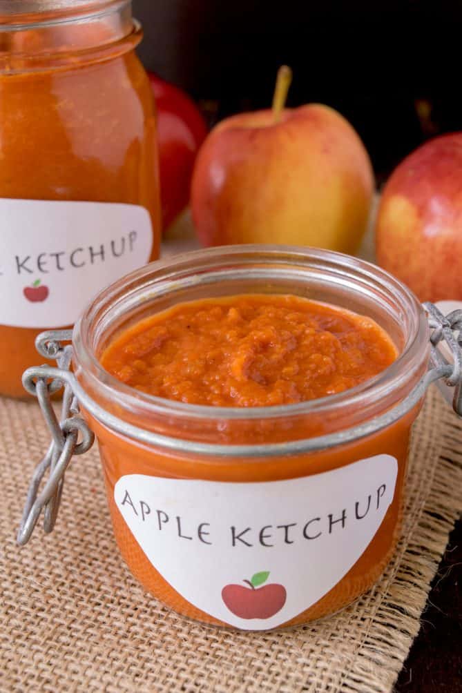 Vibrant red ketchup in a jar with fresh apples behind