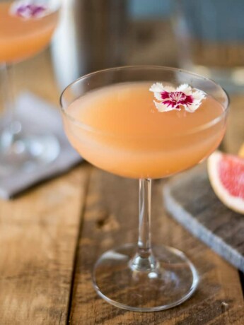 A coupe champagne glass of April Showers cocktail with a flower and grapefruit wedges