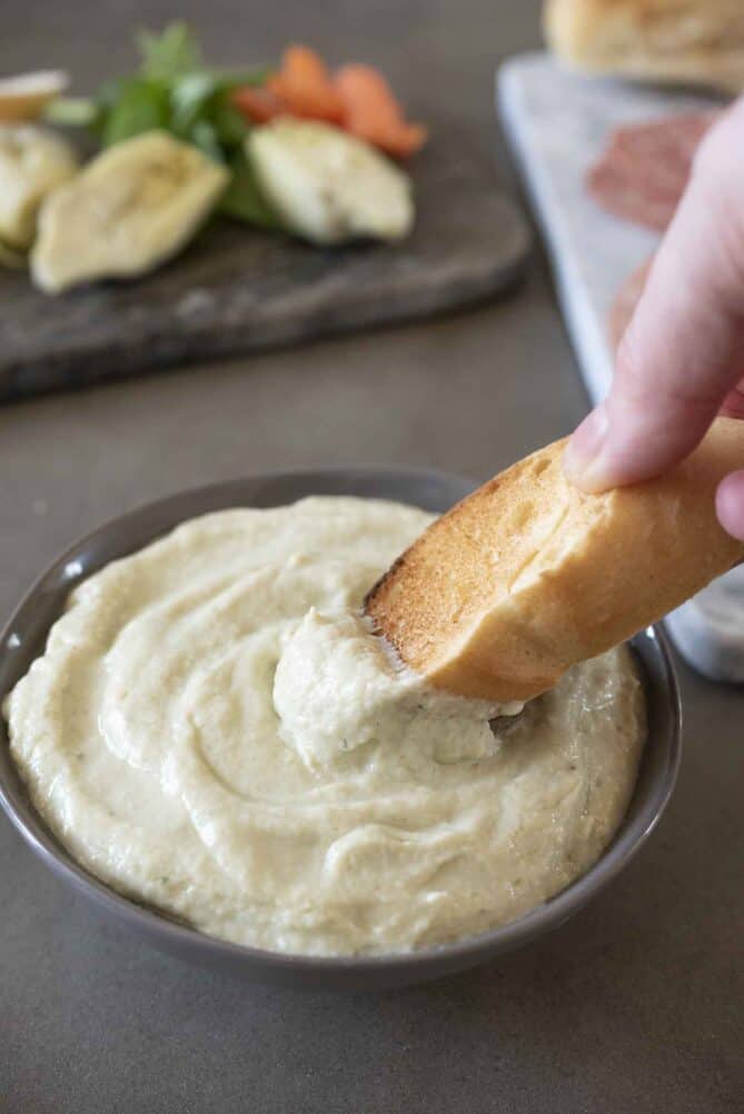 Dipping a toasted crostini into artichoke dip