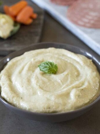 Artichoke cream in a bowl with fresh artichokes behind