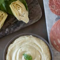 Artichoke cream spread served in a bowl with artichoke hears, carrots, mortadella and salami on a board