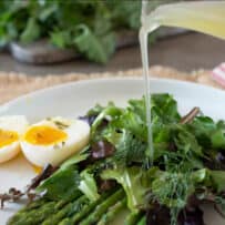 Asparagus herb salad on a plate with a boiled egg cut in half, drizzling a vinaigrette dressing
