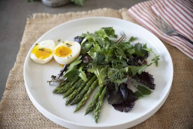Green and purple salad on a round plate with asparagus and egg