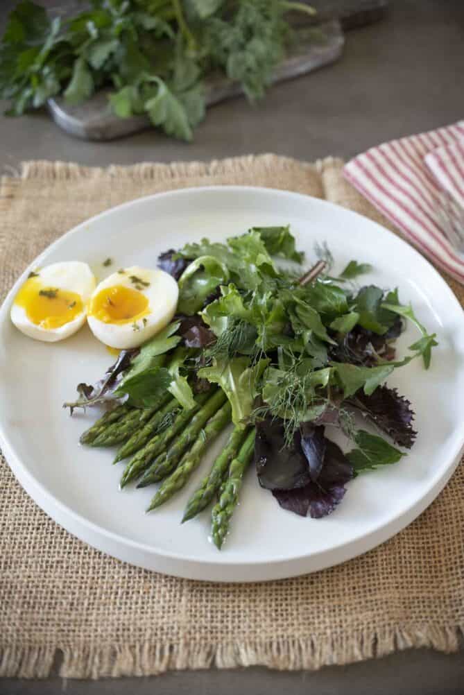 Mixed salad greens with asparagus and a boiled egg on a white plate