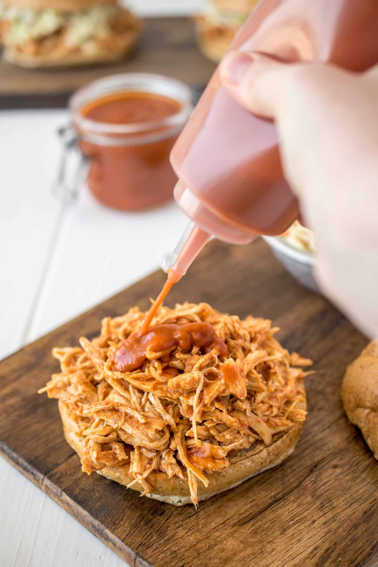 Drizzling extra barbecue sauce over pulled chicken sandwich